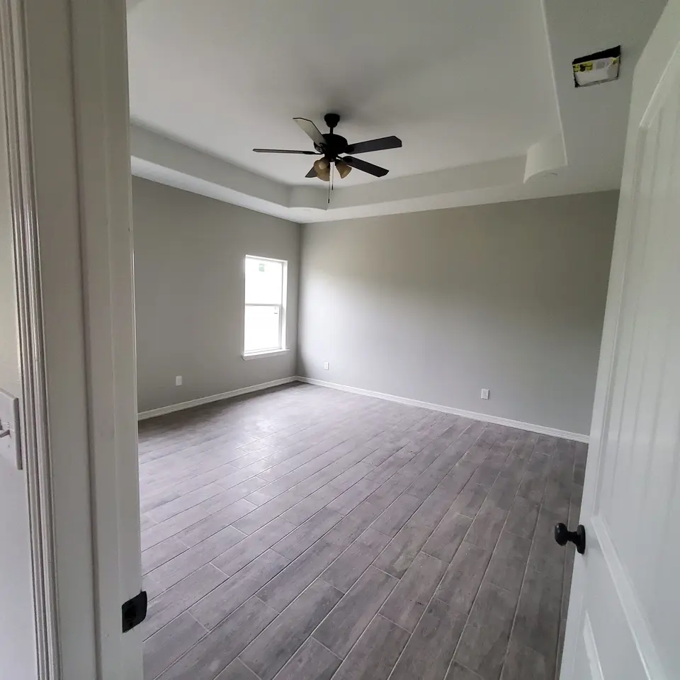 Finished Better Builders bedroom with a tray ceiling, ceiling fan, neutral walls, natural light, and wood-look tile flooring.
