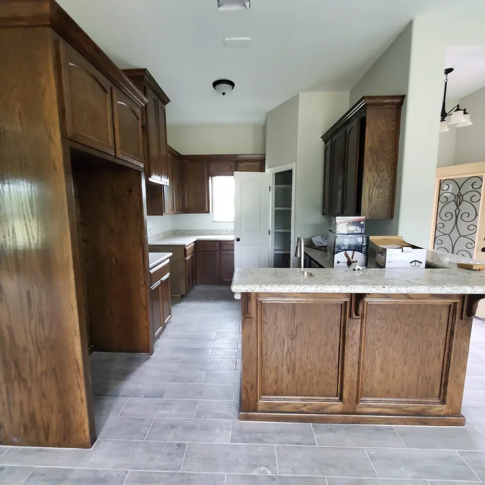 Completed Better Builders kitchen with custom wood cabinetry, granite counters, a peninsula, and coordinated wood-look tile flooring.