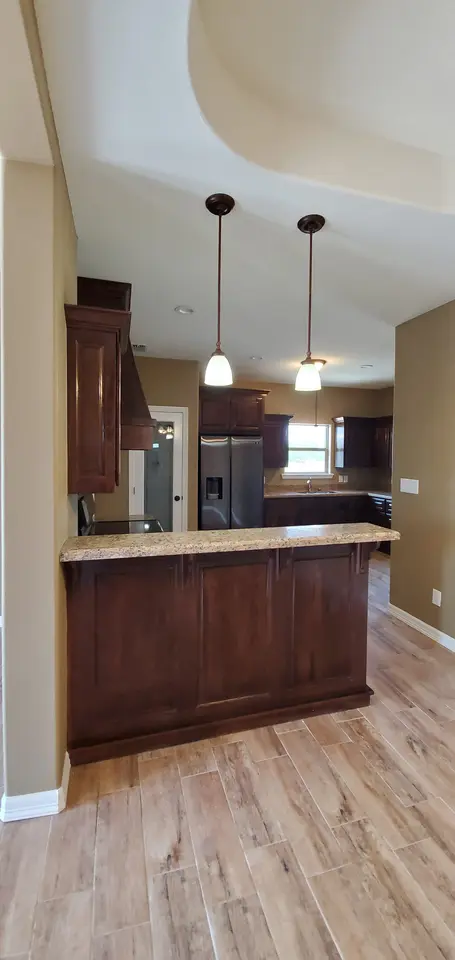 Finished Better Builders kitchen with custom wood cabinetry, granite surfaces, pendant lighting, and an open island layout.