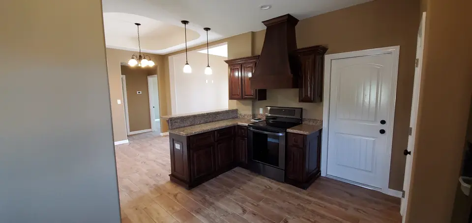 Finished Better Builders kitchen with custom wood cabinets, granite counters, a raised serving bar, and pendant lighting.
