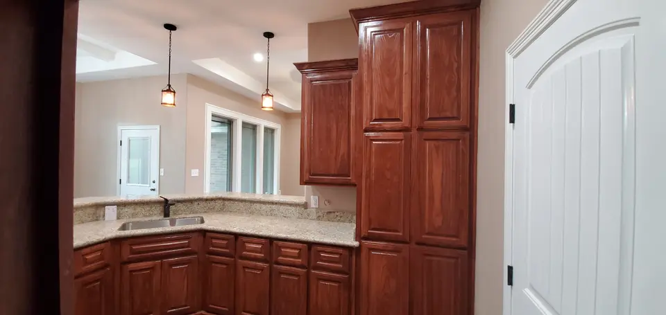Finished Better Builders kitchen with custom wood cabinetry, granite counters, a double-basin sink, pendant lighting, and tall storage.