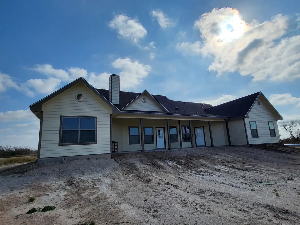Rear elevation of a Better Builders home near completion with light horizontal siding, dark trim, multiple gables, a chimney, and a long covered porch.