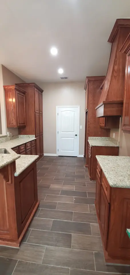 Finished Better Builders kitchen with custom wood cabinets, granite work surfaces, recessed lighting, and coordinated tile flooring.