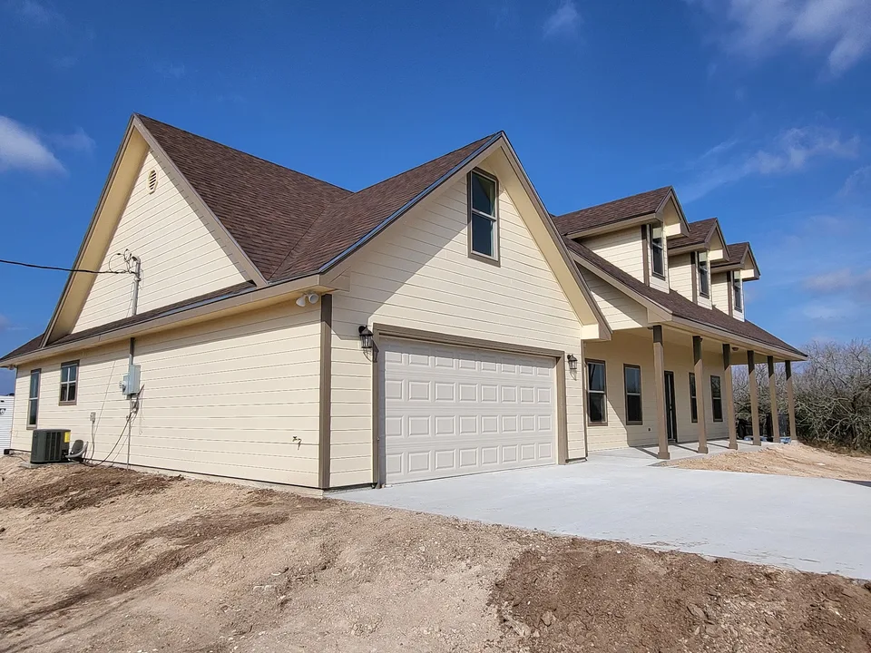 Three-quarter exterior of a Better Builders home near completion with light horizontal siding, a two-car garage, multiple gables and dormers, and a long covered porch.