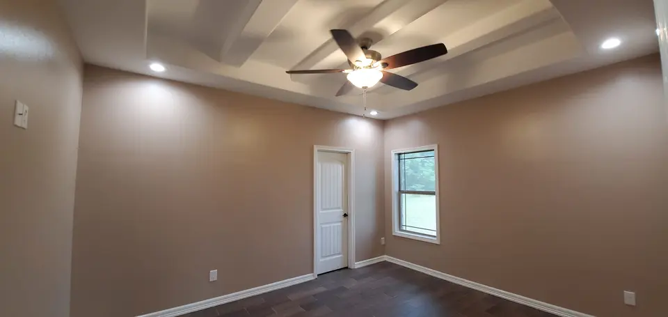 Finished Better Builders bedroom with a decorative tray ceiling, ceiling fan, recessed lights, neutral walls, and wood-look tile flooring.