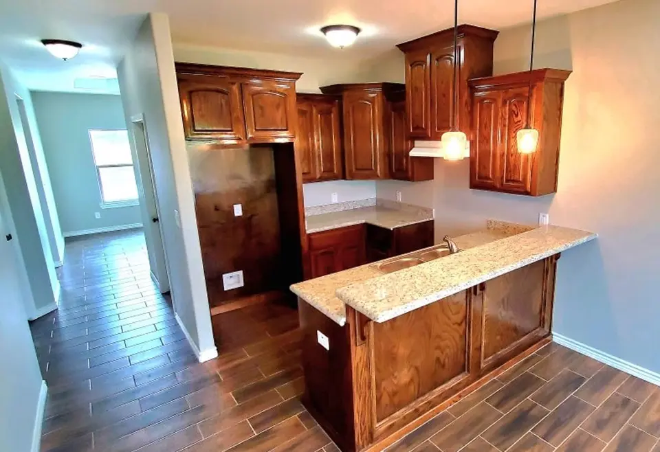 Finished Better Builders kitchen with dark wood cabinetry, granite island, and pendant lights.
