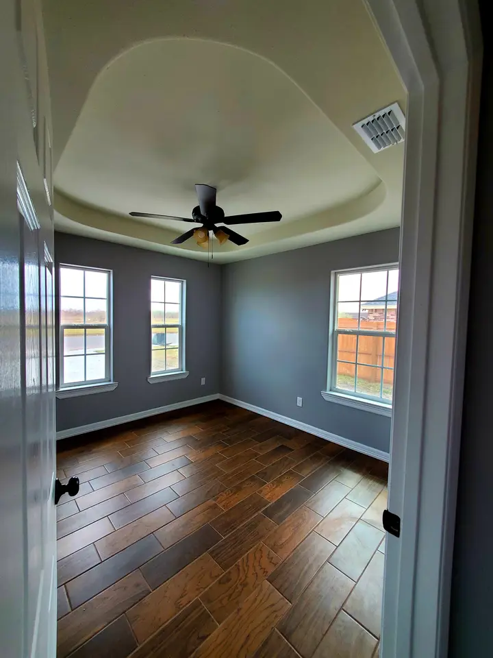 Finished bedroom with wood-look tile flooring, natural light, and a decorative tray ceiling.