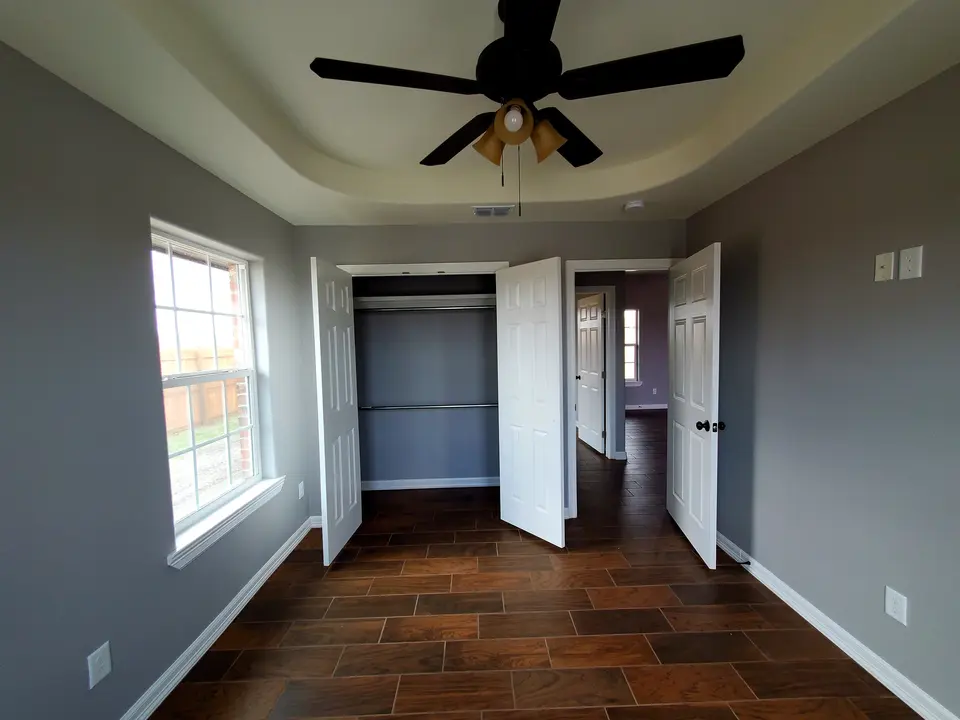 Finished bedroom with wood-look tile, a tray ceiling, and open double doors to the closet.