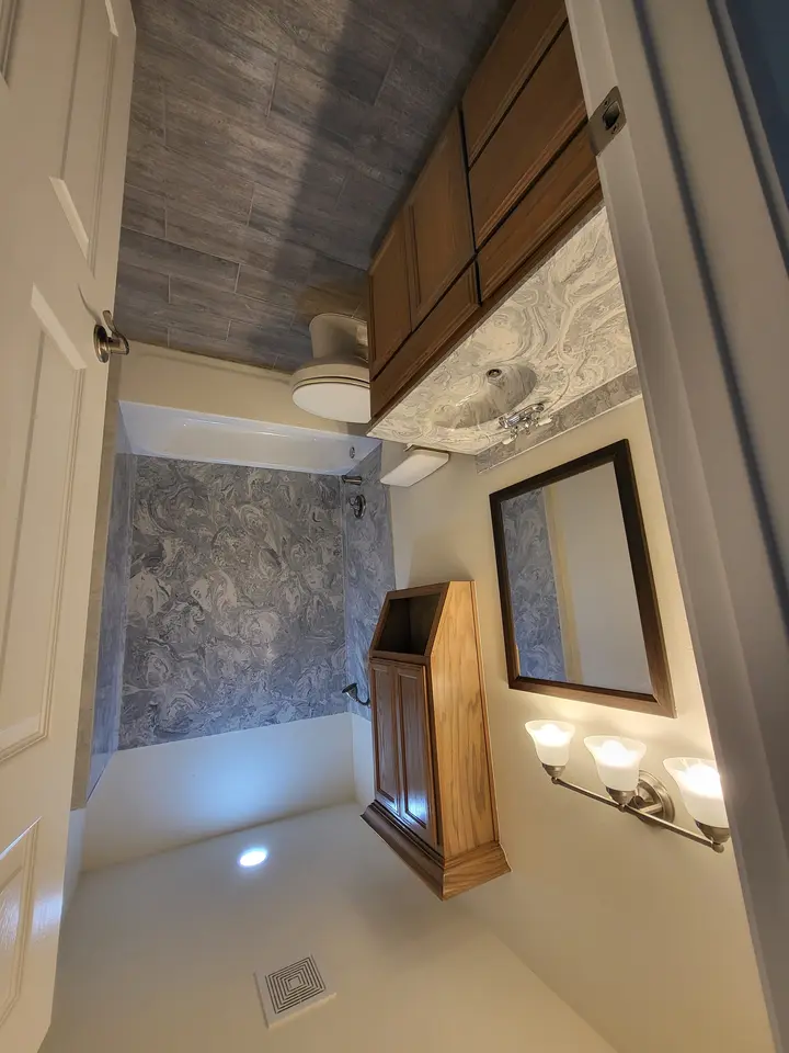 Finished bathroom with custom stone-look tile, wood cabinetry, and coordinated vanity surfaces.
