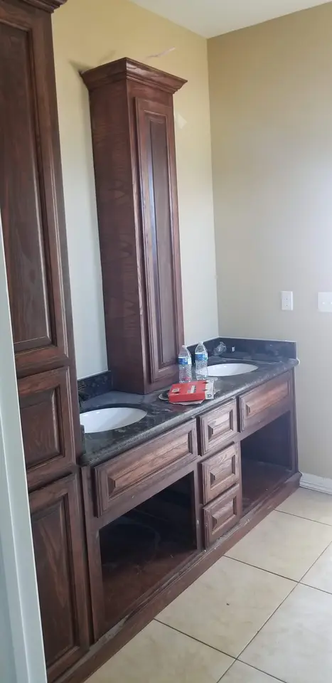 Tall custom wood bathroom cabinetry and a dual-sink vanity during final installation.