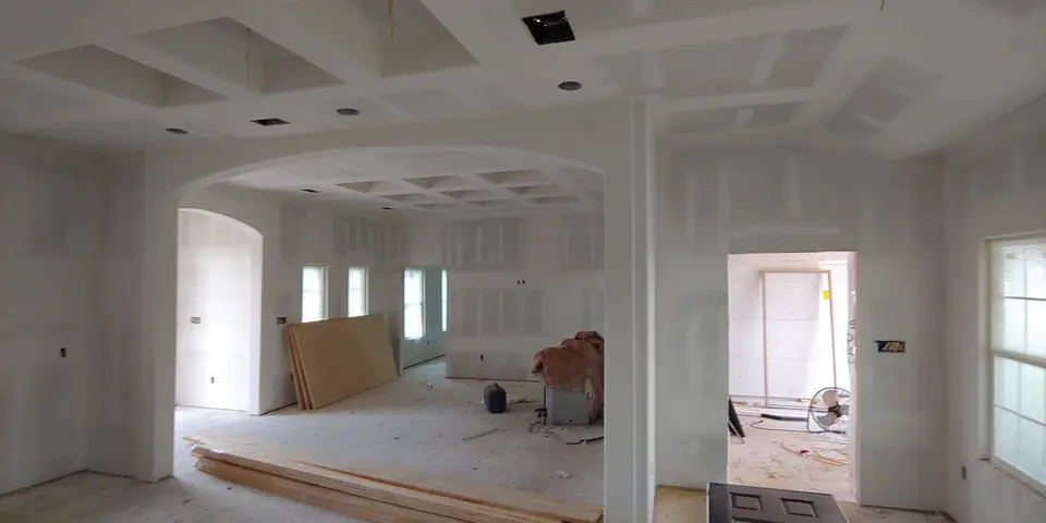 Wide open-plan interior with drywall finishing and custom ceiling details underway.