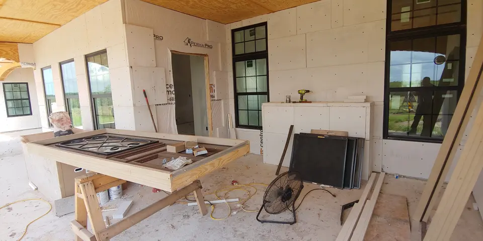 Covered rear patio with an outdoor fireplace and large windows during construction.