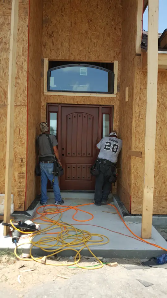 Craftsmen installing a wood front door beneath an arched transom opening in a framed Better Builders home.