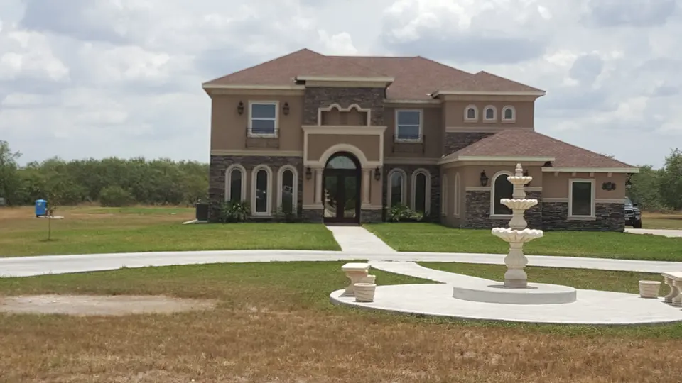 Large completed Better Builders estate home with masonry detailing, circular driveway, lawn, and decorative fountain.