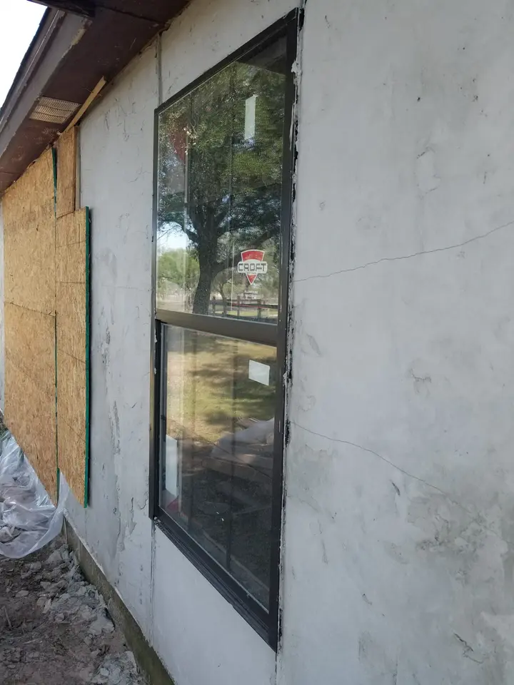 Tall black-framed exterior window surrounded by fresh stucco finish work on a Better Builders home.
