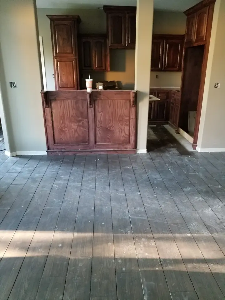 Built-in stained wood cabinet bar overlooking wood-look flooring during interior finish work.