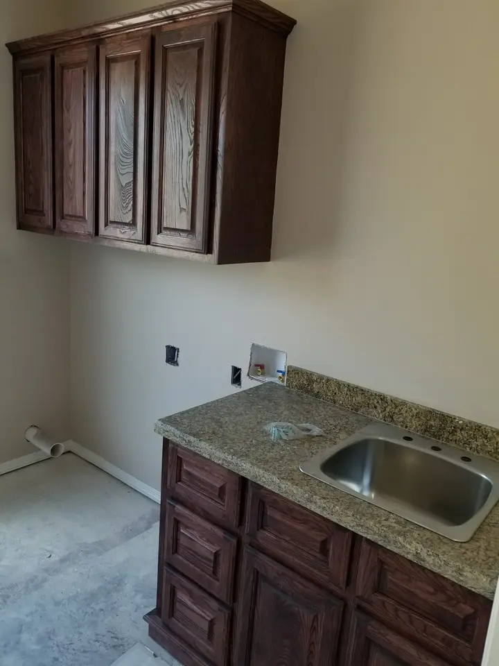 Granite utility sink counter with stained wood upper and lower storage cabinetry inside a Better Builders home.