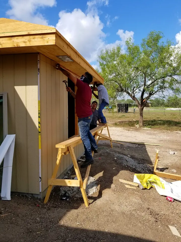 Two craftsmen installing vertical exterior siding beneath the roof overhang of a Better Builders home.