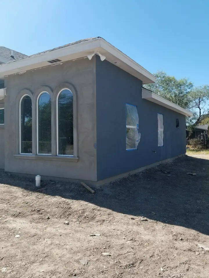 Side exterior of a Better Builders home with three tall arched windows and fresh gray stucco finish work.