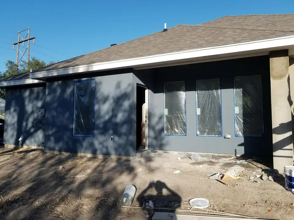 Front exterior of a dark stucco Better Builders home with grouped windows and entry finish work underway.