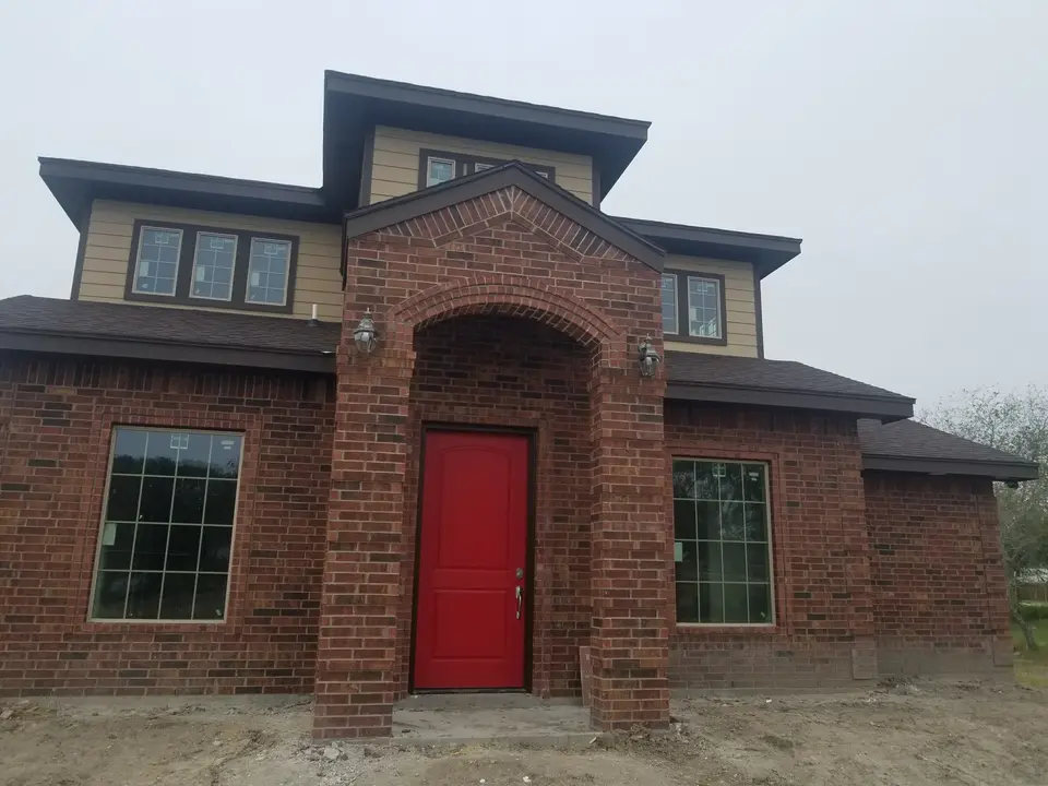 Completed brick Better Builders home with a tall arched entrance, red front door, and symmetrical window groupings.