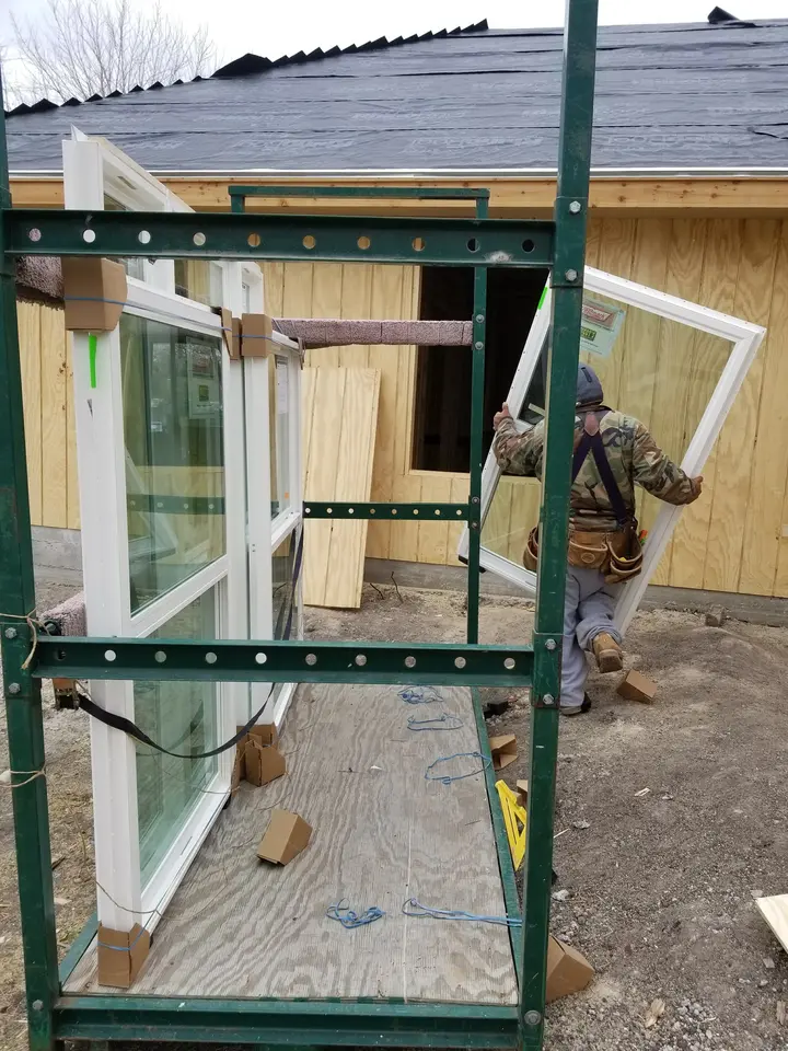 Craftsman positioning a large white-framed window at the front of a Better Builders home under construction.