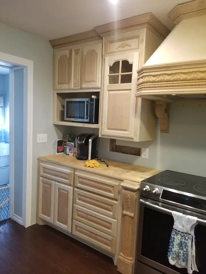 Cream-colored custom kitchen cabinetry, decorative range hood, microwave, and appliance wall inside a Better Builders home.
