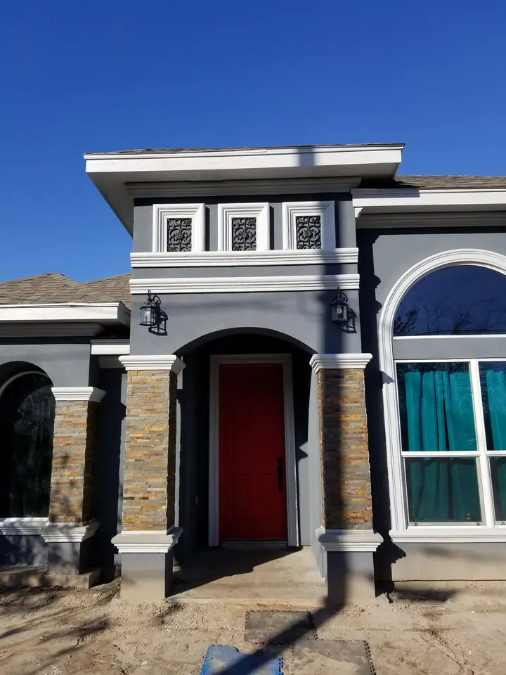 Modern dark-gray Better Builders home entry with a red door, stone columns, decorative trim, and a large arched window.