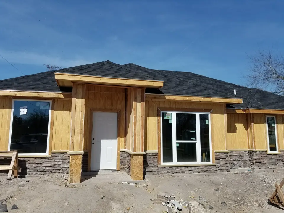 Front of a Better Builders home under construction with stone-clad entry columns, installed windows, and roof complete.