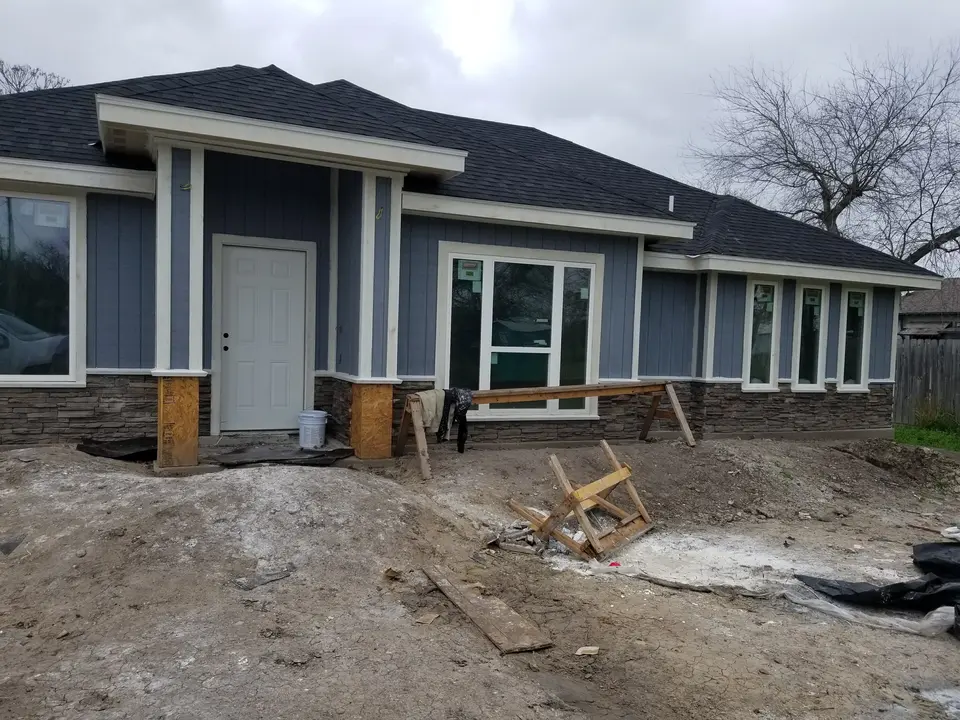 Front elevation of a Better Builders home with blue vertical siding, white trim, installed windows, and entry work in progress.