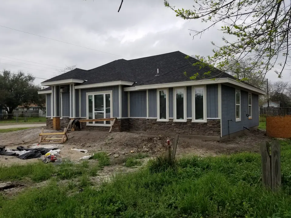 Wide front and side view of a blue-sided Better Builders home with white trim, completed roofing, and installed windows.