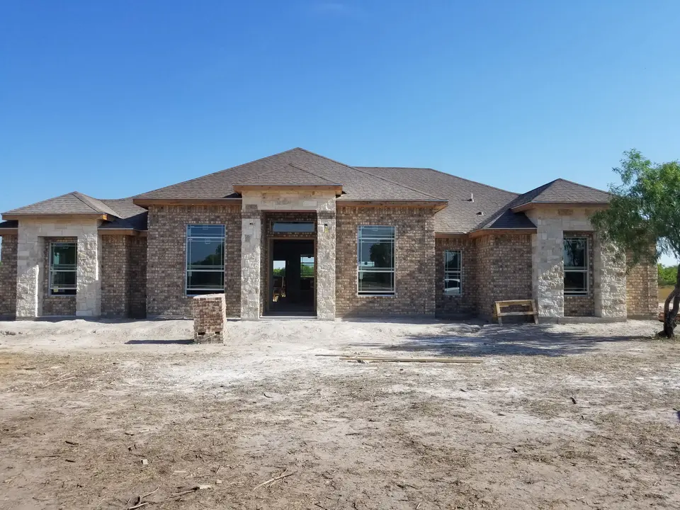 Wide front view of a Better Builders brick home with limestone accents, installed windows, and completed roofing.