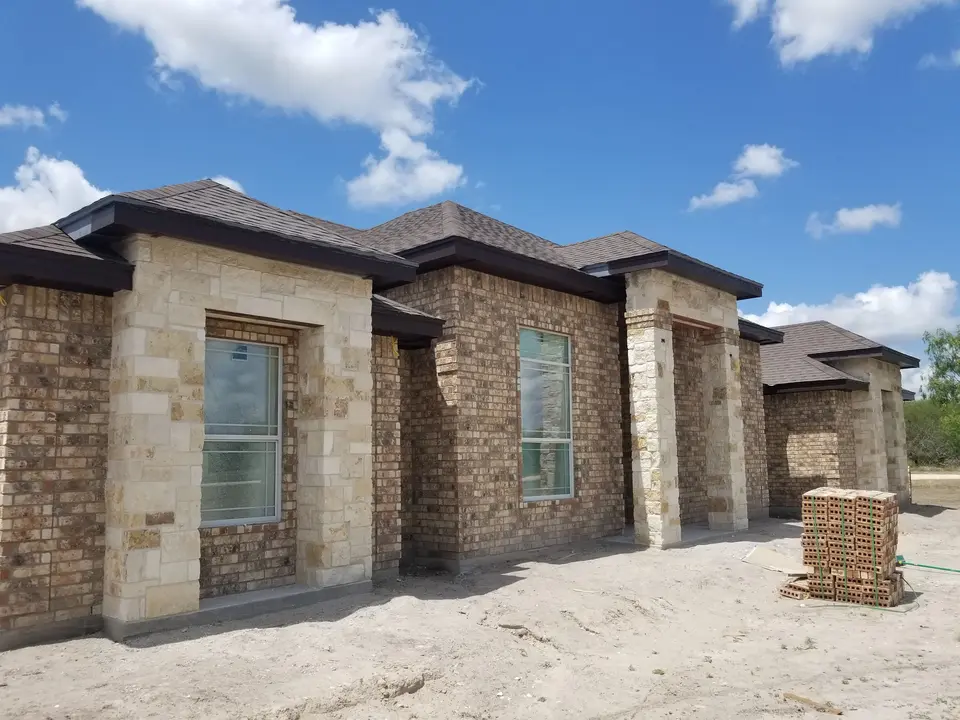 Angled exterior view of a Better Builders home with brick walls, limestone window surrounds, and layered rooflines.