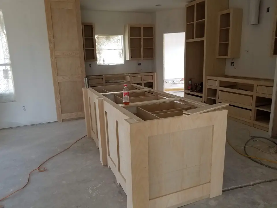 Unfinished custom wood kitchen cabinets and a large island being installed inside a Better Builders home.