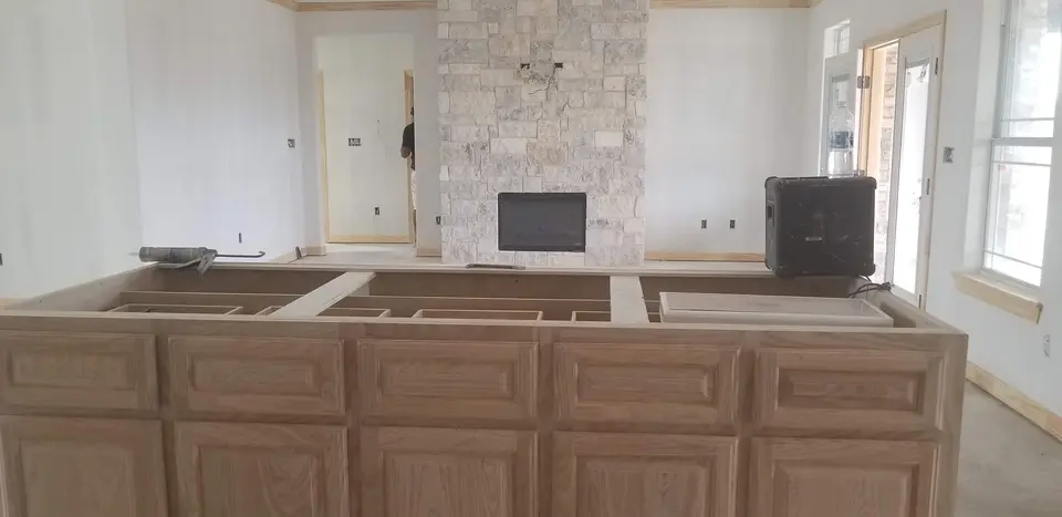 Custom wood kitchen island cabinetry facing a light-stone fireplace in an open Better Builders living area.