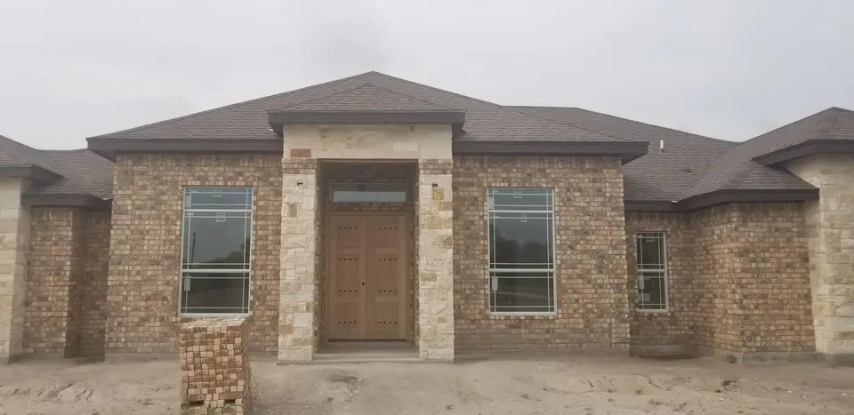 Front of a Better Builders brick home with limestone entry columns, tall windows, and a custom wood front door.