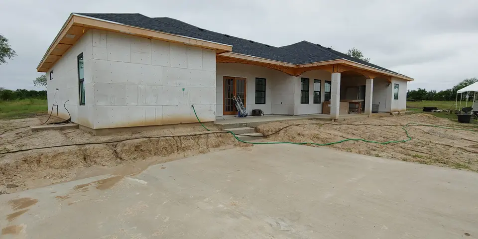 Wide rear and side view of a Better Builders home with roofing, windows, wall sheathing, and covered patio framing underway.