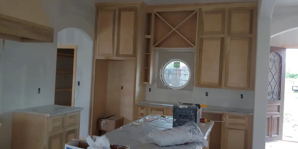 Natural wood custom kitchen cabinetry with built-in wine storage surrounding a round window during installation.