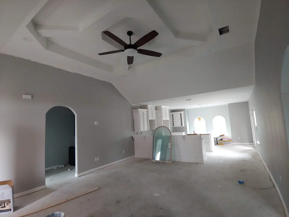 Open Better Builders living area with a sculpted tray ceiling, ceiling fan, arched doorway, and kitchen cabinetry during finish work.