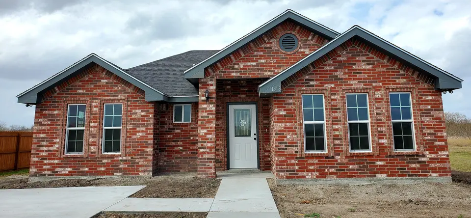 Front exterior of a completed Better Builders red-brick home with layered gables, tall grouped windows, and a centered entry.