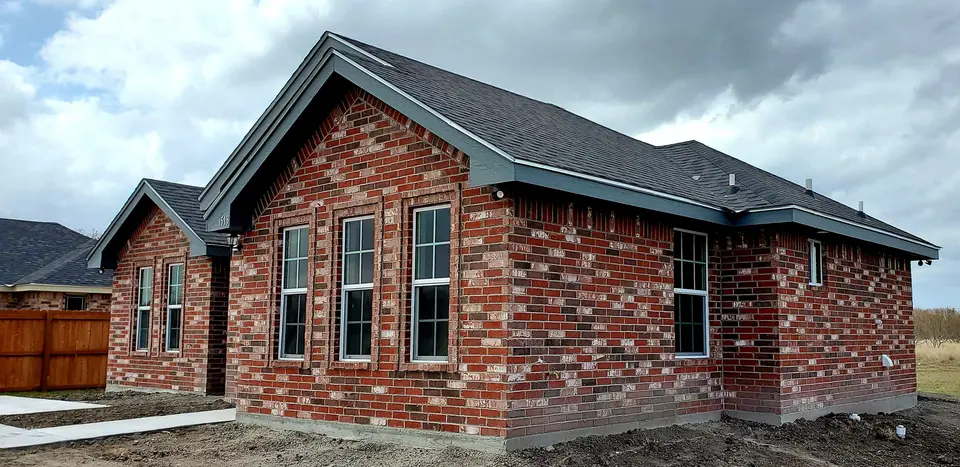 Angled front and side view of a completed Better Builders red-brick residence with tall windows and layered roofing.