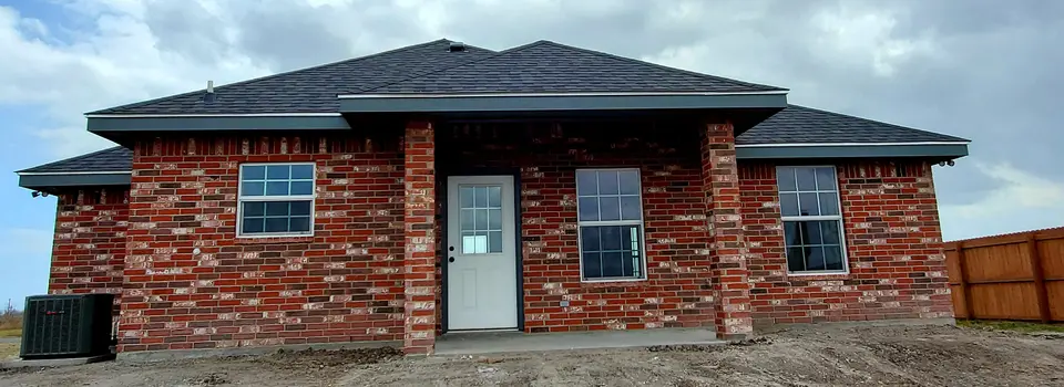 Rear exterior of a completed Better Builders red-brick home with a wide roofline, back entry, windows, and fenced yard.