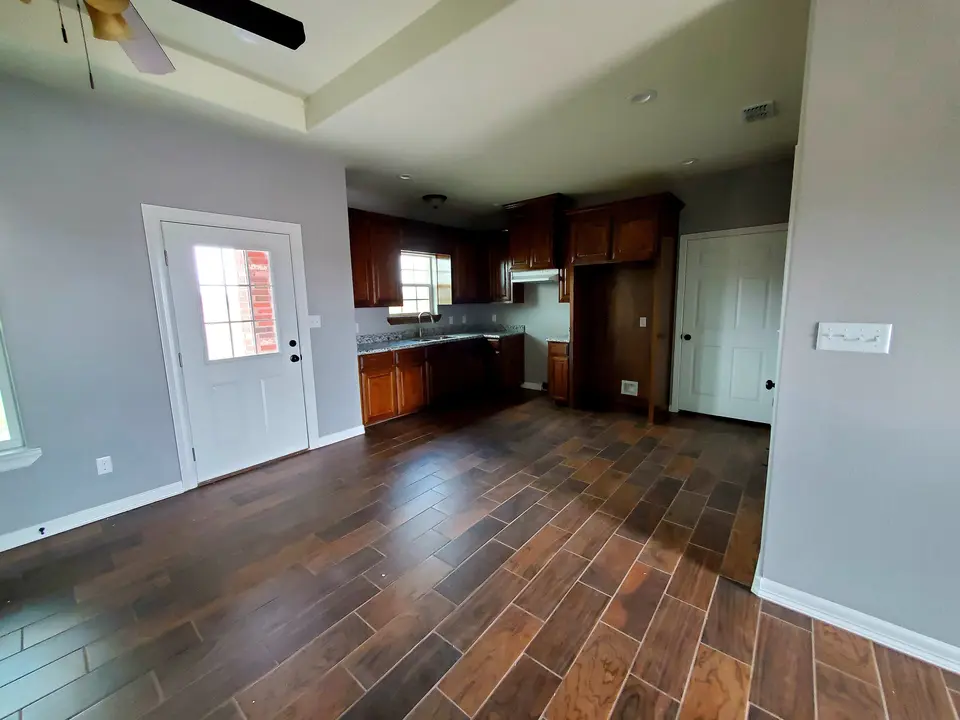 Open kitchen and living area with dark wood cabinetry, wood-look tile, gray walls, and recessed lighting in a completed Better Builders home.