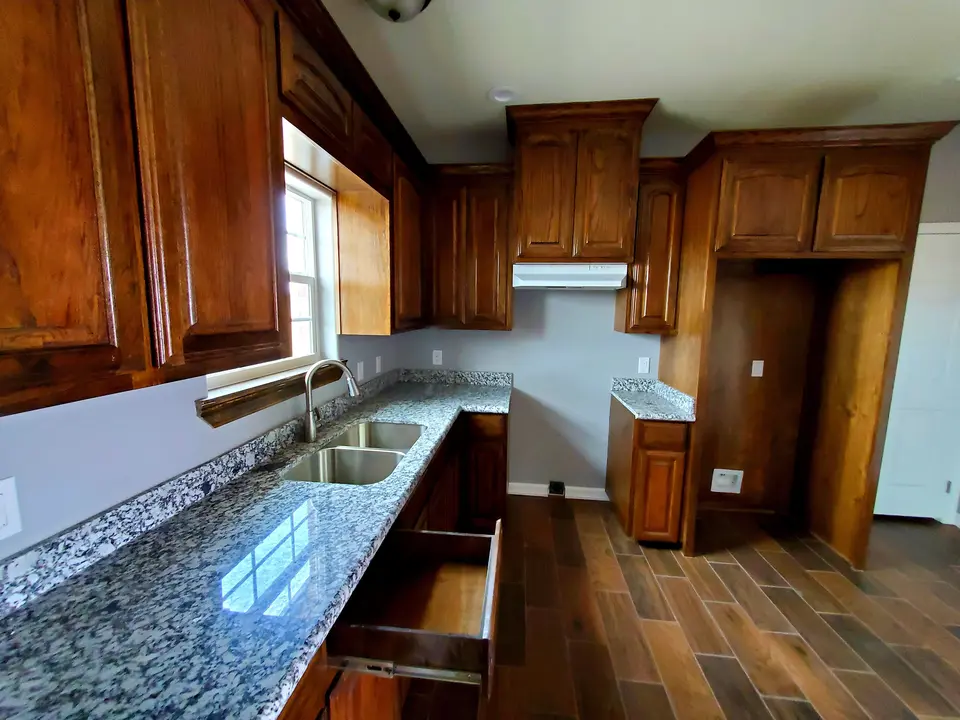 Close finished kitchen view with granite countertop, double-basin sink, window, and custom dark wood cabinetry.