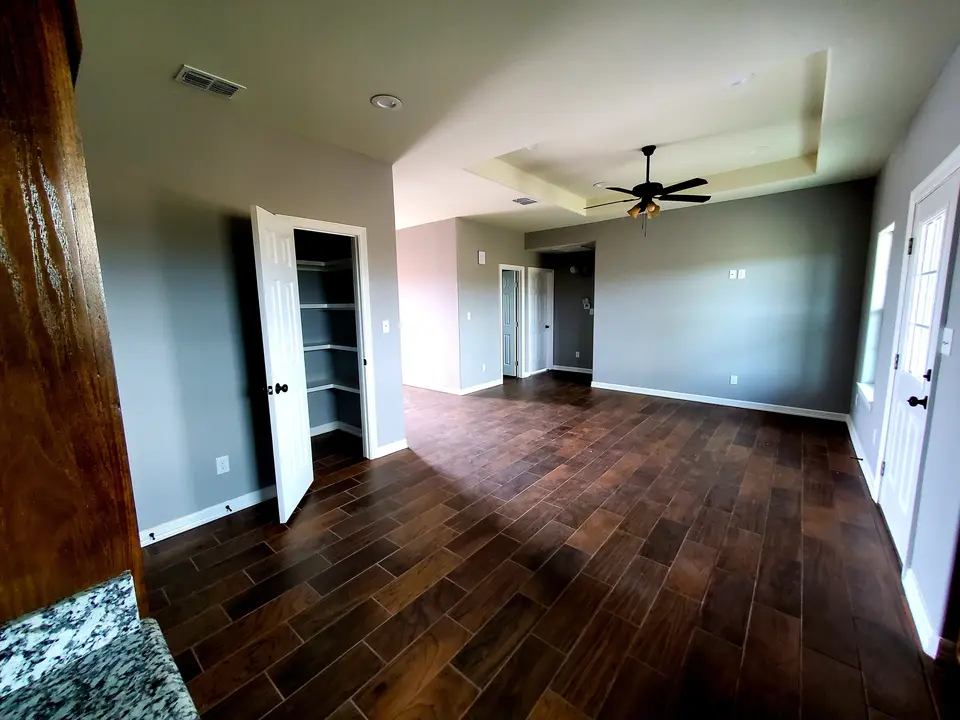 Finished living room with a layered tray ceiling, ceiling fan, gray walls, white trim, and wood-look tile.