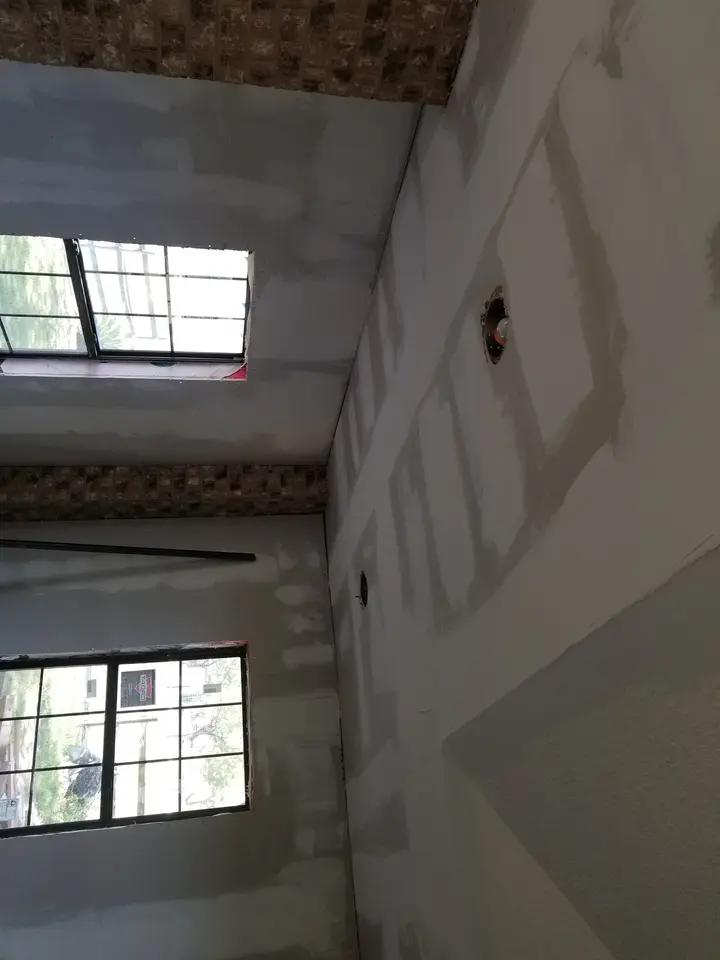 Construction-stage Better Builders room with taped drywall, black-framed windows, recessed-light openings, and exposed brick ceiling accents.