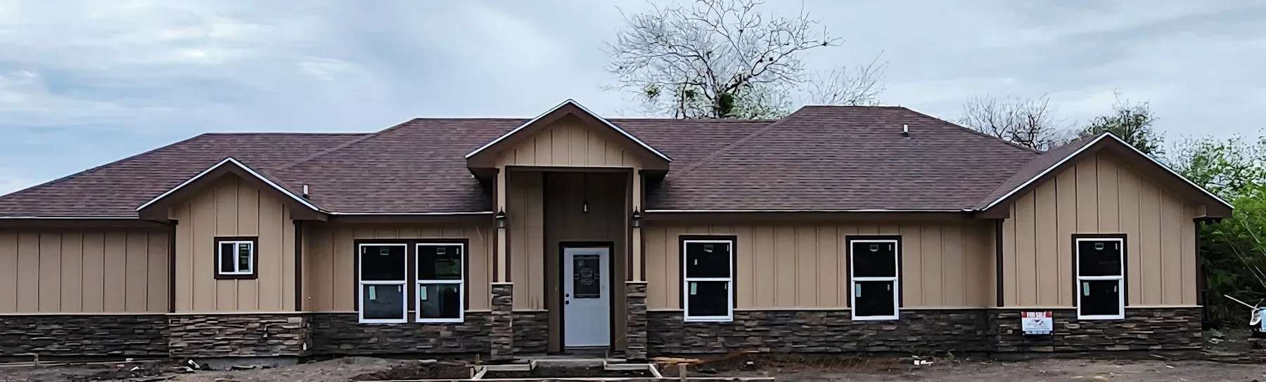 Panoramic construction-stage front view of the Lucero Street home with roofing, siding, stone accents, windows, and entry finishes installed.